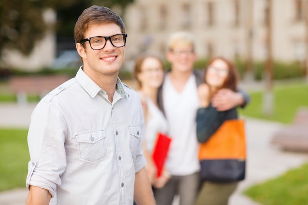 vacaciones de verano, educación, campus y concepto adolescente - adolescente sonriente con anteojos con compañeros de clase en la parte de atrás