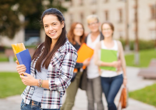 vacaciones de verano, educación, campus y concepto adolescente - adolescente sonriente con carpetas y compañeros de clase en la parte de atrás