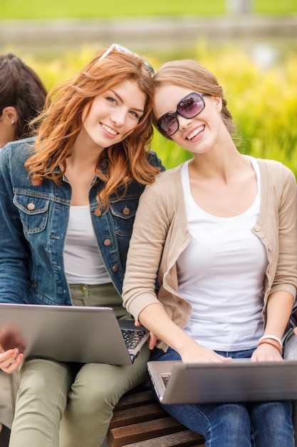 vacaciones de verano, educación, campus, tecnología y concepto adolescente - dos estudiantes con computadoras portátiles