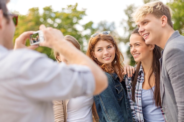 vacaciones de verano, electrónica y concepto adolescente - grupo de adolescentes sonrientes tomando fotos con cámara digital afuera