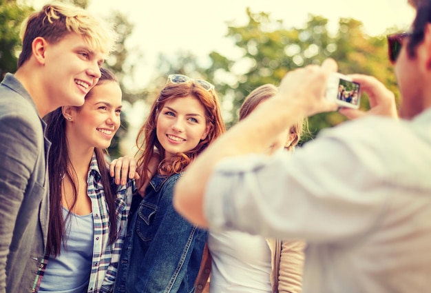 vacaciones de verano, electrónica y concepto adolescente - grupo de adolescentes sonrientes tomando fotos con cámara digital afuera