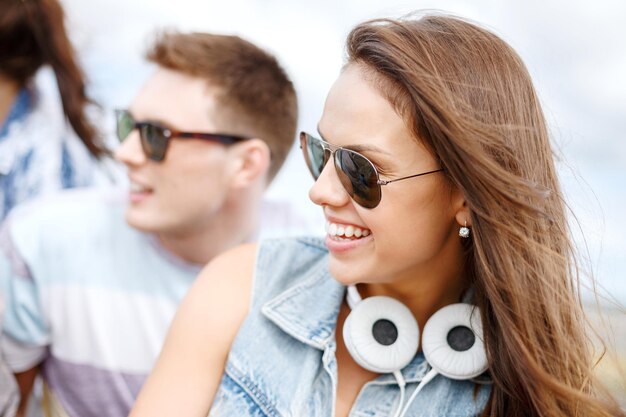 vacaciones de verano, gente y concepto de felicidad - adolescente sonriente con gafas de sol al aire libre con amigos