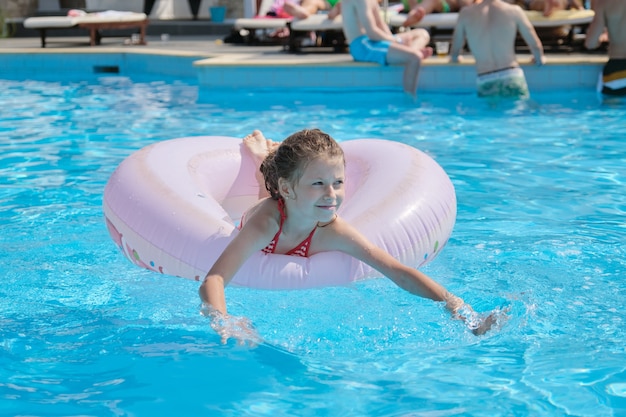Vacaciones de verano, niña descansando en el anillo de natación en la piscina al aire libre, hotel balneario