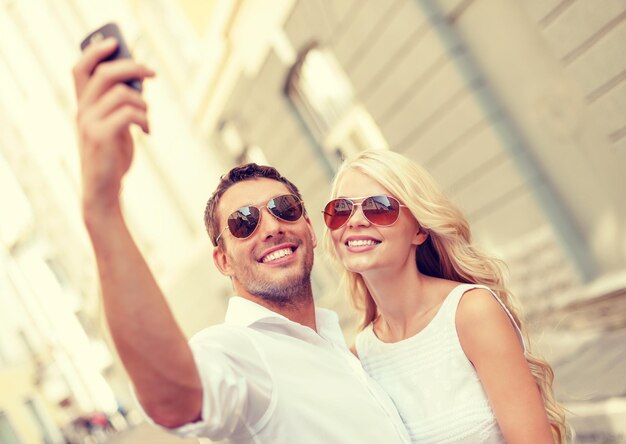 vacaciones de verano, tecnología, amor, relación y concepto de citas - pareja sonriente tomando fotos con un smartphone en la ciudad