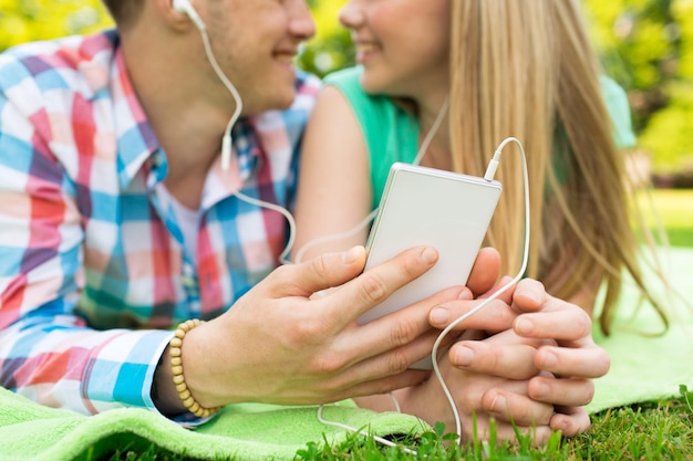 vacaciones de verano, tecnología y concepto de personas - cerca de una pareja sonriente con smartphone y auriculares escuchando música en el parque