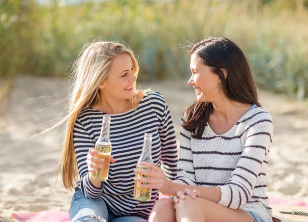 vacaciones de verano, vacaciones, celebración y concepto de la gente - adolescentes felices o mujeres jóvenes bebiendo cerveza o limonada en la playa