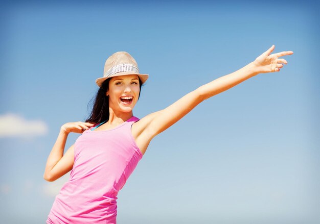 Vacaciones de verano y vacaciones - chica con sombrero mostrando la dirección en la playa