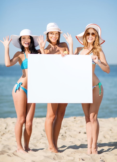 Vacaciones de verano y vacaciones - chicas en bikini sosteniendo una pizarra en blanco en la playa