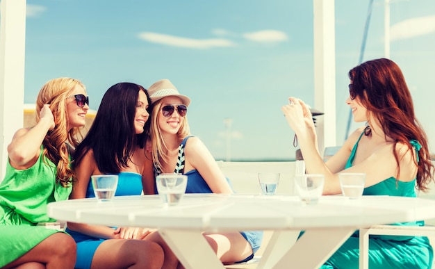 vacaciones de verano y vacaciones - chicas tomando fotos con cámara digital en un café en la playa