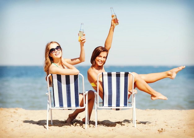 vacaciones de verano y vacaciones - chicas tomando el sol y bebiendo en las sillas de playa