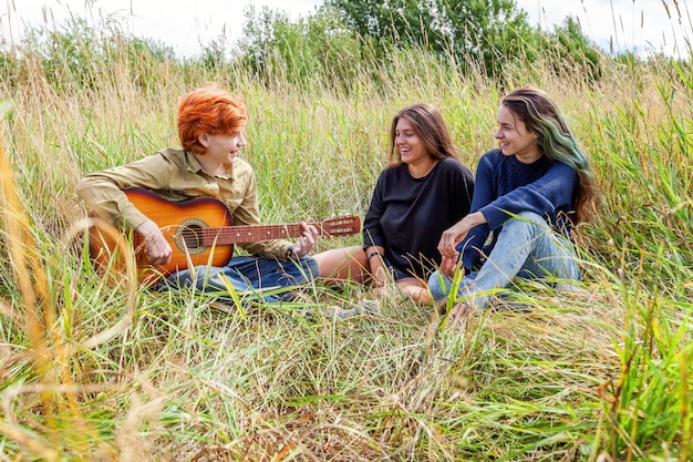 Vacaciones de verano vacaciones música concepto de gente feliz. grupo de tres amigos chico y dos chicas con guitarra cantando canción divirtiéndose juntos al aire libre. picnic con amigos en viaje por carretera en la naturaleza.