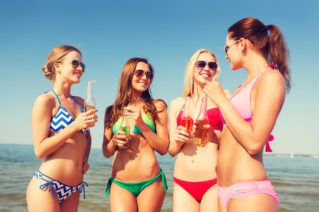 vacaciones de verano, vacaciones, viajes y concepto de personas - grupo de mujeres jóvenes sonrientes tomando el sol y bebiendo en la playa