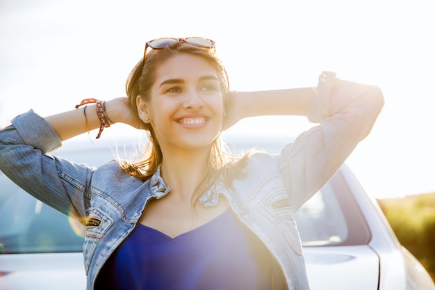 Foto vacaciones de verano, vacaciones, viajes, viaje por carretera y concepto de personas - feliz sonriente adolescente o mujer joven cerca del coche en la playa