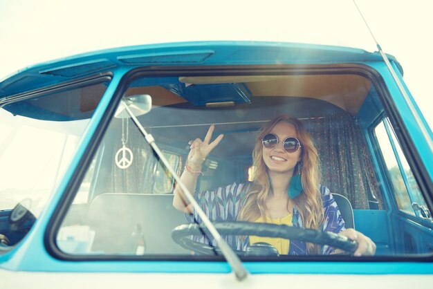 Foto vacaciones de verano, viaje por carretera, vacaciones, viajes y concepto de personas - joven hippie sonriente conduciendo un minivan y mostrando un gesto de paz