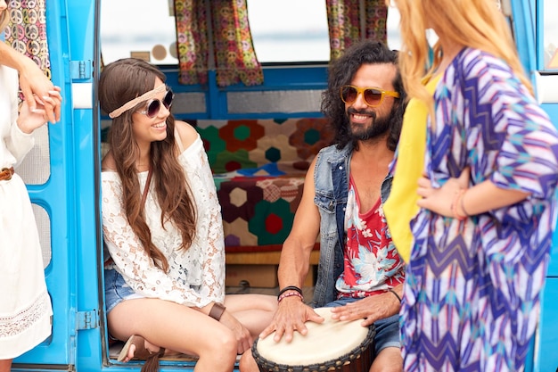 vacaciones de verano, viaje por carretera, viajes y gente concepto - felices jóvenes amigos hippie con tom-tom tambor divirtiéndose y tocando música en el coche minivan