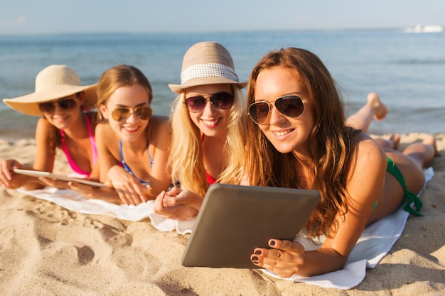 vacaciones de verano, viajes, tecnología y concepto de personas - grupo de mujeres sonrientes en gafas de sol con computadoras de tablet pc tiradas en la playa