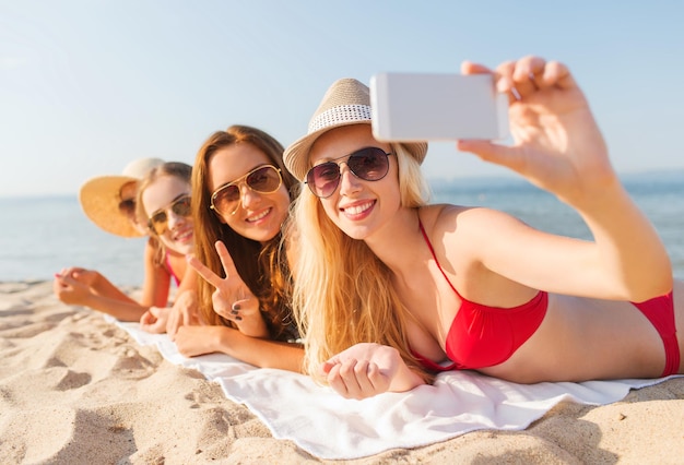 vacaciones de verano, viajes, tecnología y concepto de personas - grupo de mujeres sonrientes con gafas de sol haciendo selfie con smartphone en la playa