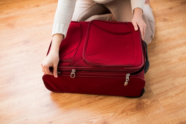 Foto vacaciones de verano, viajes, turismo y concepto de objetos: cierre de una mujer que empaca y cierra una bolsa de viaje para las vacaciones