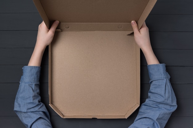 Vaciar la caja abierta de pizza en manos de los niños. Superficie negra. Vista superior. Copia espacio