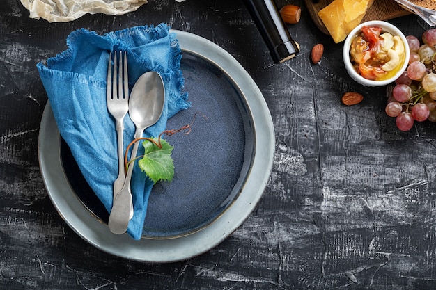 Vaciar placa azul que sirve con cuchara tenedor en el marco de los ingredientes de los alimentos Cocina mediterránea, aperitivo, aperitivo, uvas, queso, vino. Plato de placa azul con espacio de copia en la mesa de hormigón oscuro.