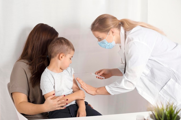Vacid 19 para crianças. Menino caucasiano sendo vacinado da Covid-19. Uma jovem médica segurando uma seringa com vacina de coronavírus. Conceito de controle de risco e infecção.