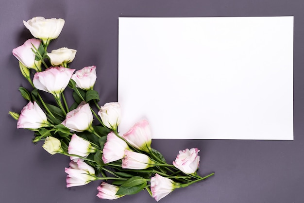 Vacie el papel y el eustoma de las flores en superficie gris con el espacio de la copia.