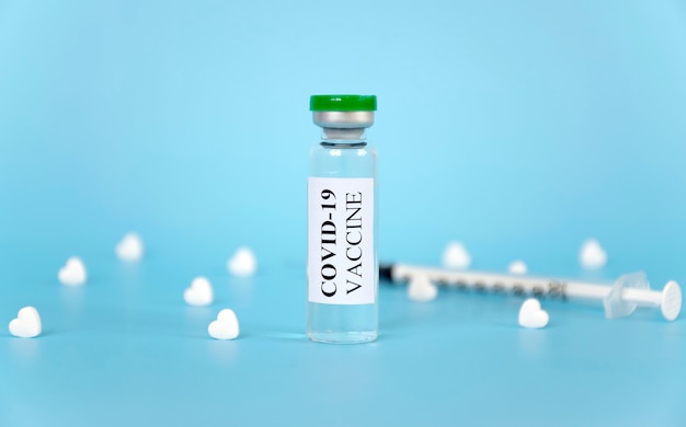 Vacina do Coronavírus COVID-19 em frasco de vidro com comprimidos em formato de coração branco e seringa na mesa azul. Prevenção mundial da pandemia.