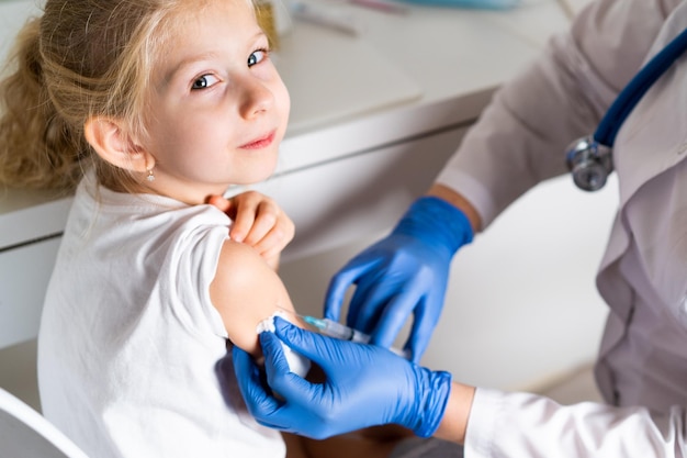 Vacinação de crianças uma garotinha em um médico marca uma injeção no braço o conceito