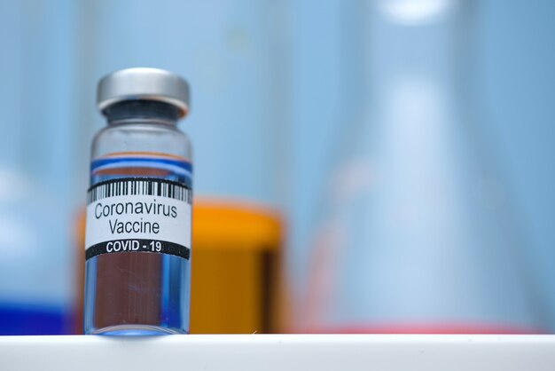 Vacuna contra el coronavirus en botella para inyección en mesa contra laboratorio médico de fondo