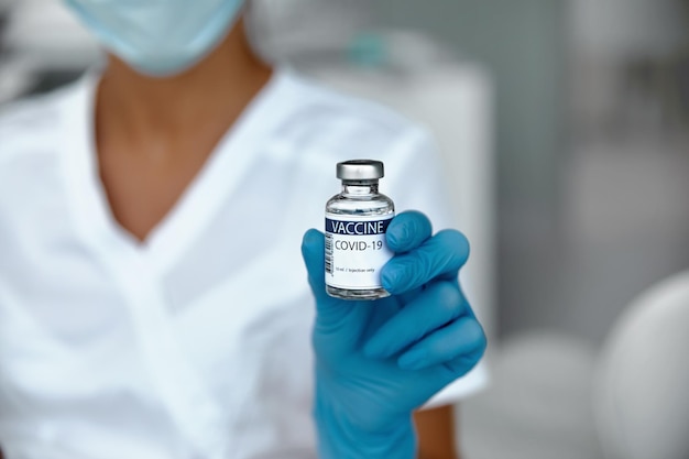 Vacuna contra el coronavirus en botella de vidrio en la mano del médico. Tarro de vacuna sobre fondo blanco en azul glovs. Concepto de vacuna de lucha contra el coronavirus.