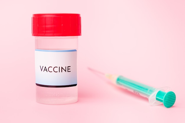 Vacuna Covid-19 en el frasco y jeringa desechable para inyección en el fondo rosa