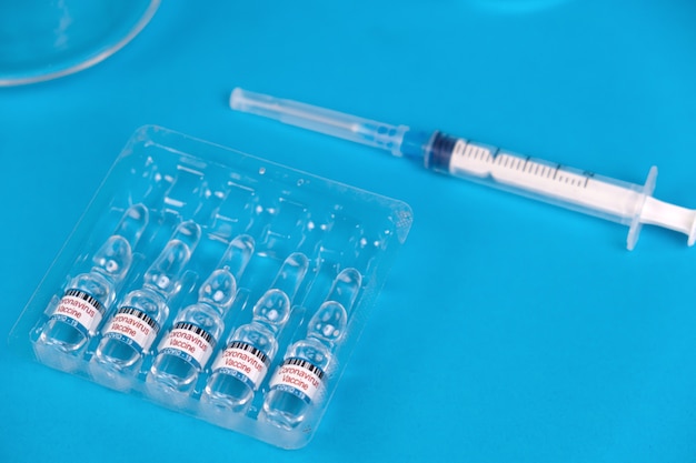 Vacuna para el tratamiento del coronavirus COVID-19 con jeringa sobre fondo azul con espacio para texto