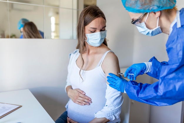 Vacunación para embarazadas. Médico administrando la inyección de la vacuna COVID -19 contra el coronavirus a una mujer embarazada. Doctor vistiendo guantes azules vacunar a la mujer embarazada joven en la clínica. Concepto de vacunación de personas.