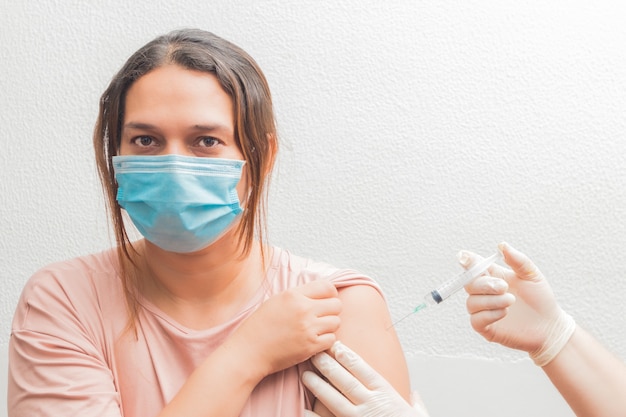 Foto vacunación, inmunización, concepto de prevención de enfermedades. mujer en mascarilla médica recibiendo la vacuna. enfermera o médico profesional que administra la inyección antiviral al paciente