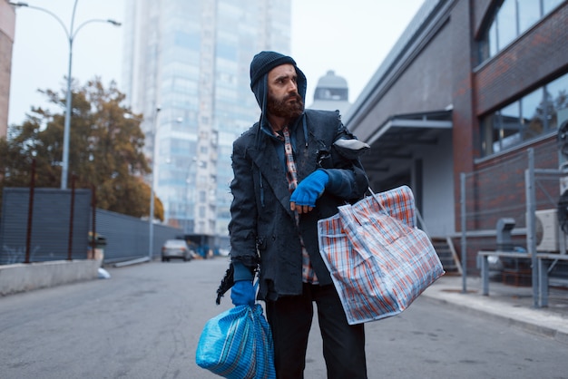 Vagabundo barbudo con bolsa en las calles de la ciudad.