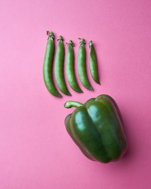 Vagens de ervilha verde em uma fileira em um fundo rosa com pimentão verde fresco com espaço de cópia, plana leigos. Vegetais organícos