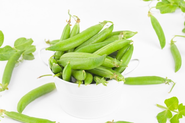 Vainas de guisantes verdes crudas orgánicas frescas en un tazón con hojas de guisantes y plantas sobre fondo blanco Proteína de frijol saludable