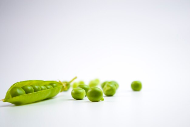 Vainas de guisantes verdes frescas con follaje sobre un fondo blanco Una vaina está abierta Los guisantes son visibles