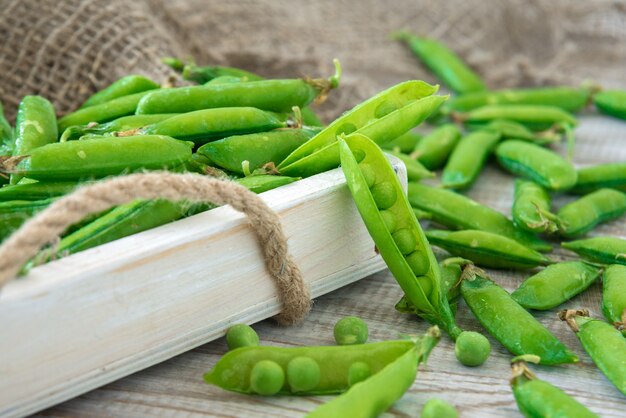 Vainas de guisantes verdes fuera en un tazón pequeño sobre una mesa de madera