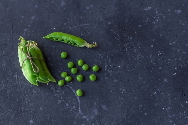 Vainas de guisantes verdes y guisantes sobre una superficie oscura