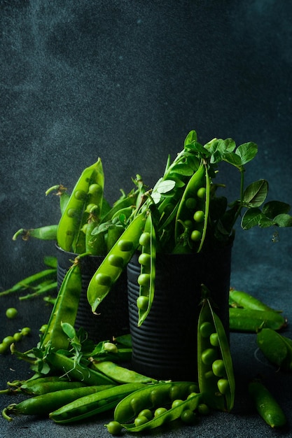 Vainas de guisantes verdes y hojas en un frasco de metal sobre un fondo oscuro vista lateral de primer plano