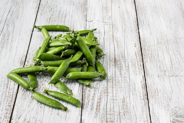 Vainas de guisantes verdes en una mesa de madera blanca