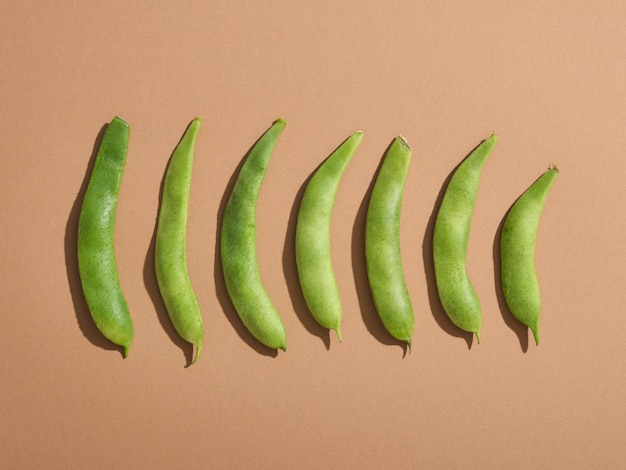 Las vainas de judías verdes se encuentran en una fila sobre una superficie de color beige pastel. Composición de naturaleza mínima.