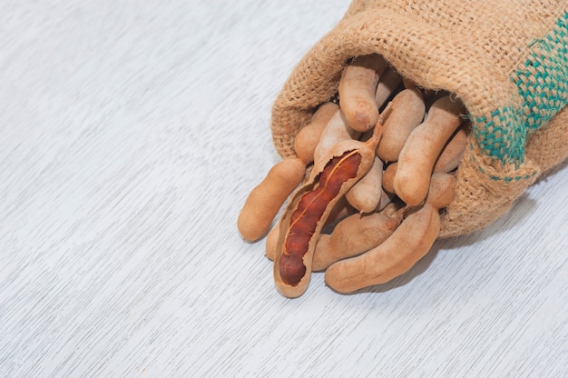 Vainas de tamarindo para la sopa de condimento de camarones Tom Yum en una pila de yute orgánico sobre fondo de madera blanco, plano