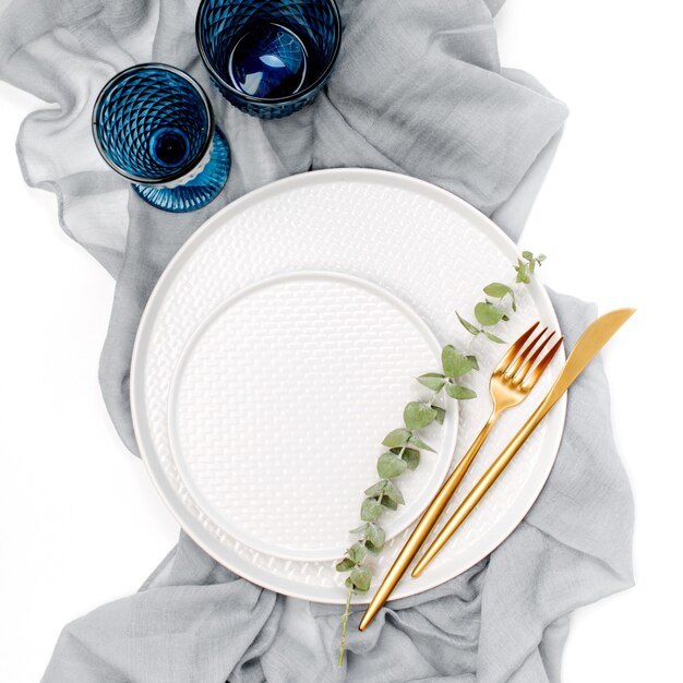 Foto vajillas y adornos para servir una mesa festiva. platos, copas de vino y cubiertos con textil decorativo gris sobre fondo blanco.