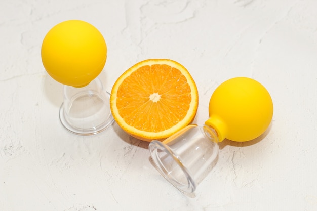 Vakuummassage-Anti-Cellulite-Becher auf grauem Hintergrund mit Orange. Selbstmassage für gesunde Haut.