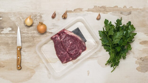 Vakuumverpacktes Rindfleisch, Messer und Gewürze auf einem Holztisch. Versiegelte Verpackung für Fleisch.