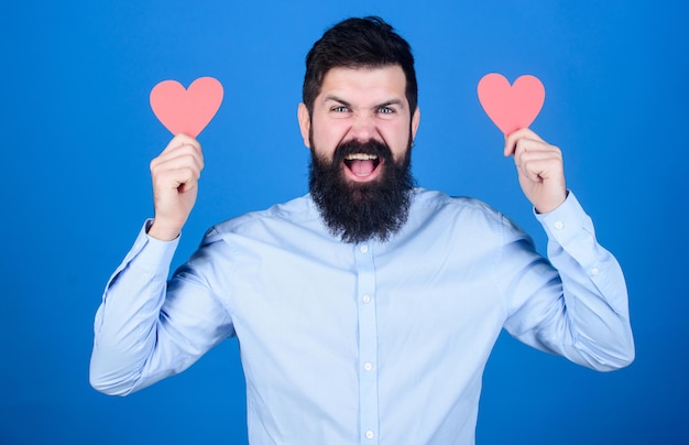 Valentines-Hasser. Bärtiger Mann mit roten Herzen. Sexy Valentinsmann mit herzförmigen Karten. Hipster mit kleinen Herzen. Anti-Valentinstag. Ausdruck seiner Gefühle.