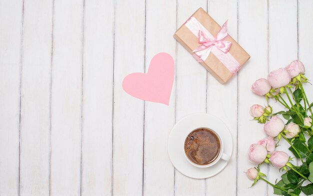 Valentinsgrußhintergrund mit Morgenkaffeetasse-Geschenkbox und -blumen auf weißem hölzernem Hintergrund