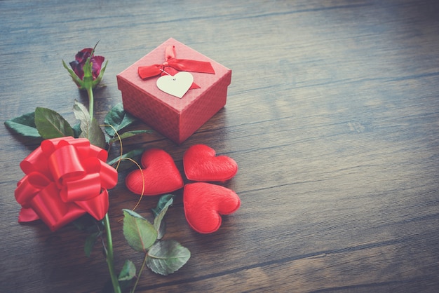 Valentinsgrußtagesgeschenkbox rot auf Holz Rote Herz-Valentinsgrußtagesrotrose Blume und Geschenkboxband beugen auf altem hölzernem